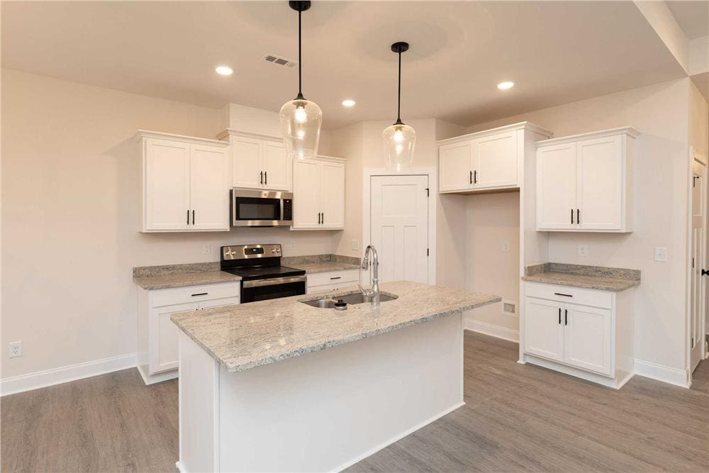Kitchen with white cabinets, granite countertops, and a center island fitted with a sink.