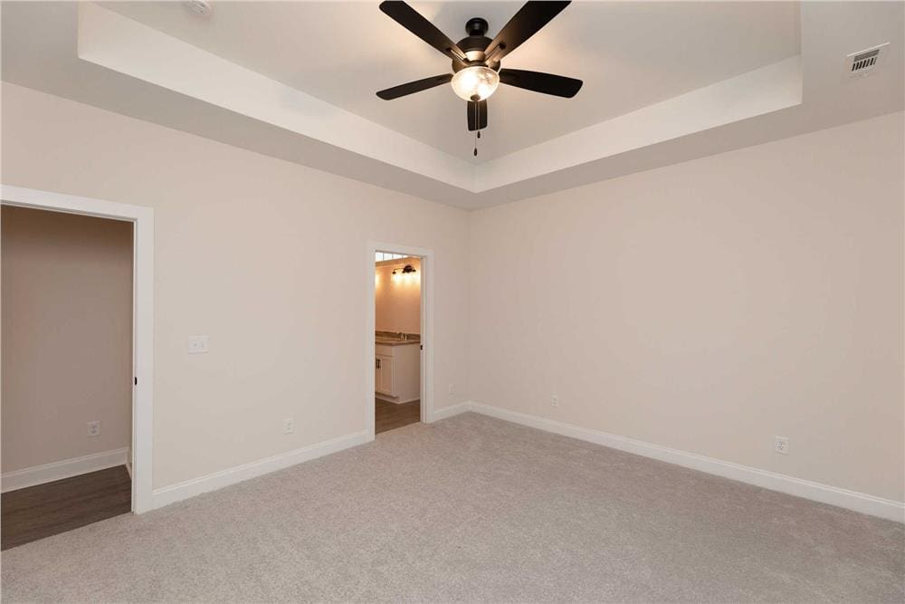 Primary bedroom with a tray ceiling, a carpeted floor, and an ensuite bathroom.
