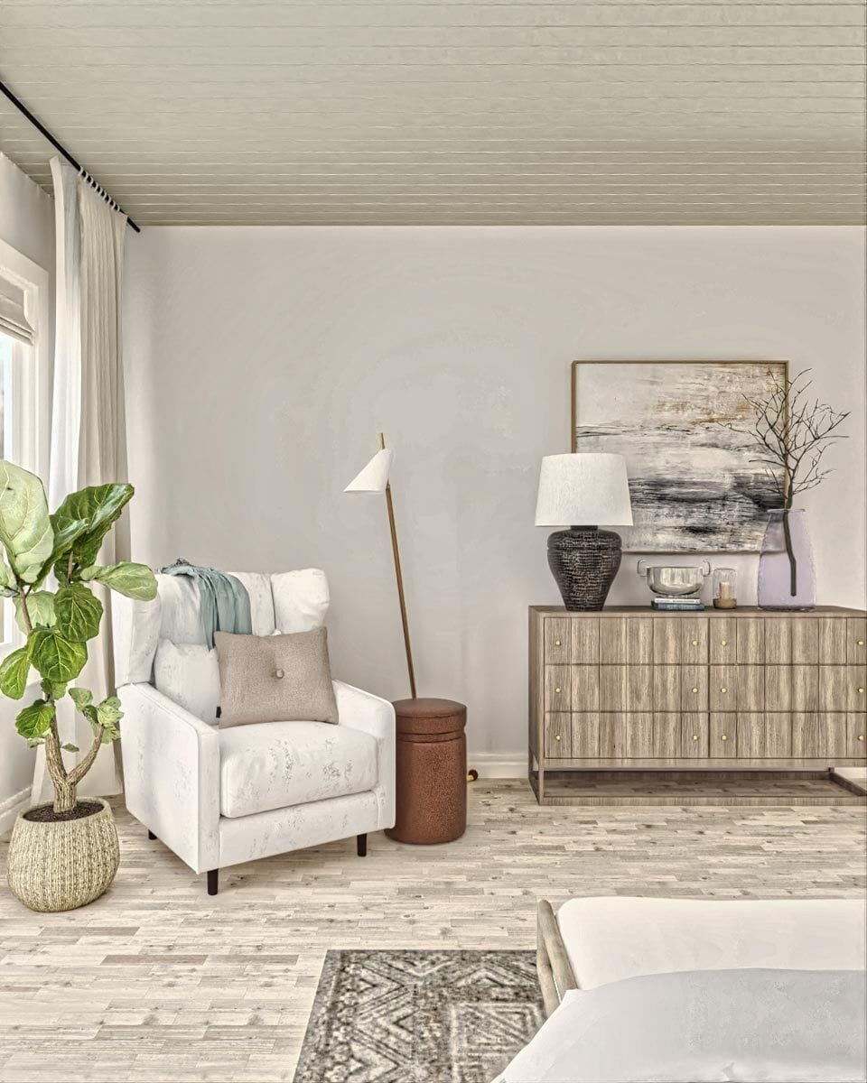 A wingback armchair and a wooden dresser topped with a table lamp and painting complete the primary bedroom.