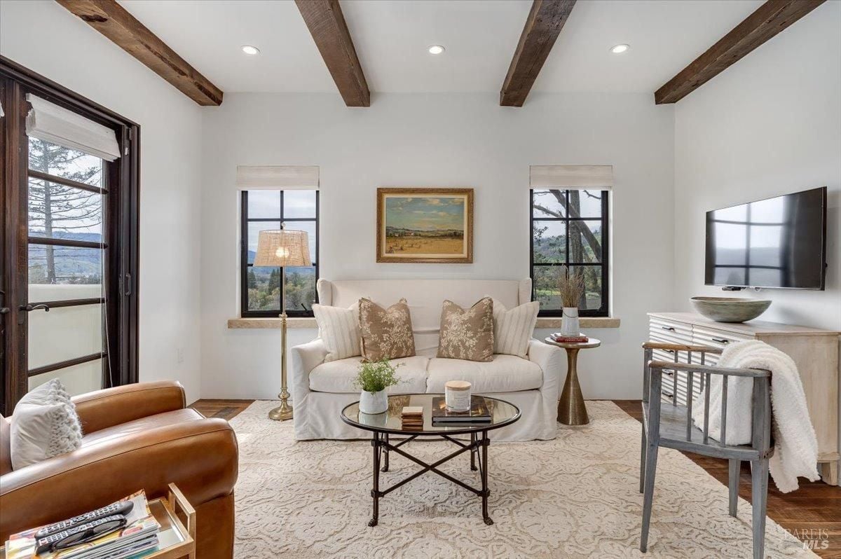 Living room with open beam ceiling and glass windows.
