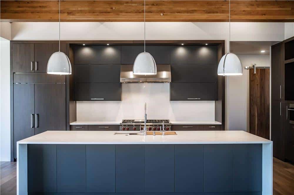 Kitchen with dark cabinets and a waterfall island topped with dome pendants.