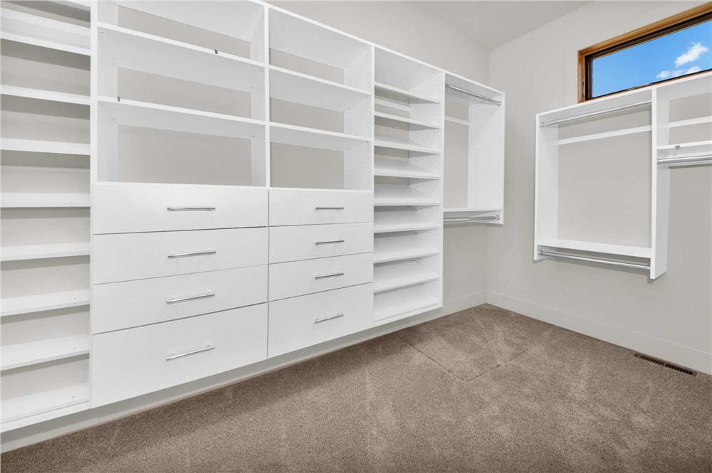 Primary walk-in closet with white built-ins and a carpeted floor.