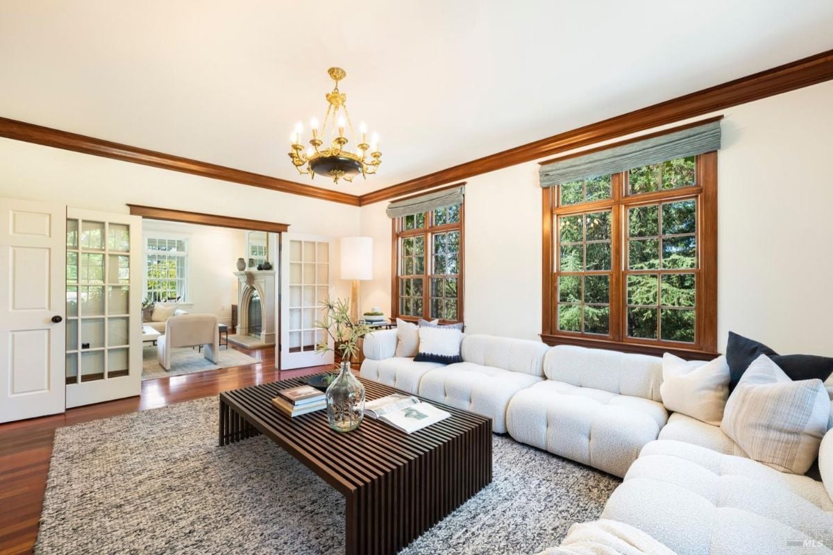 Living room with a chandelier, couches, wooden floors, French windows and a fireplace.