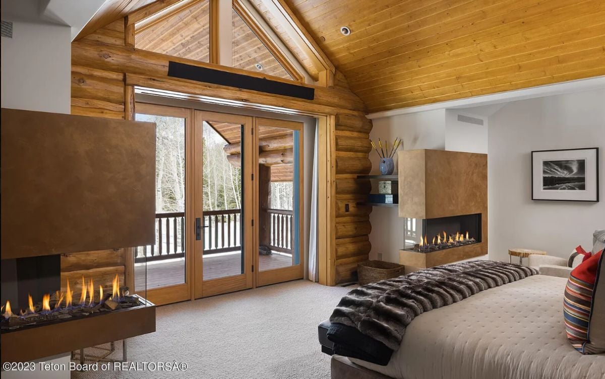Bedroom with carpet flooring, glass doors, and dual gas fireplace.