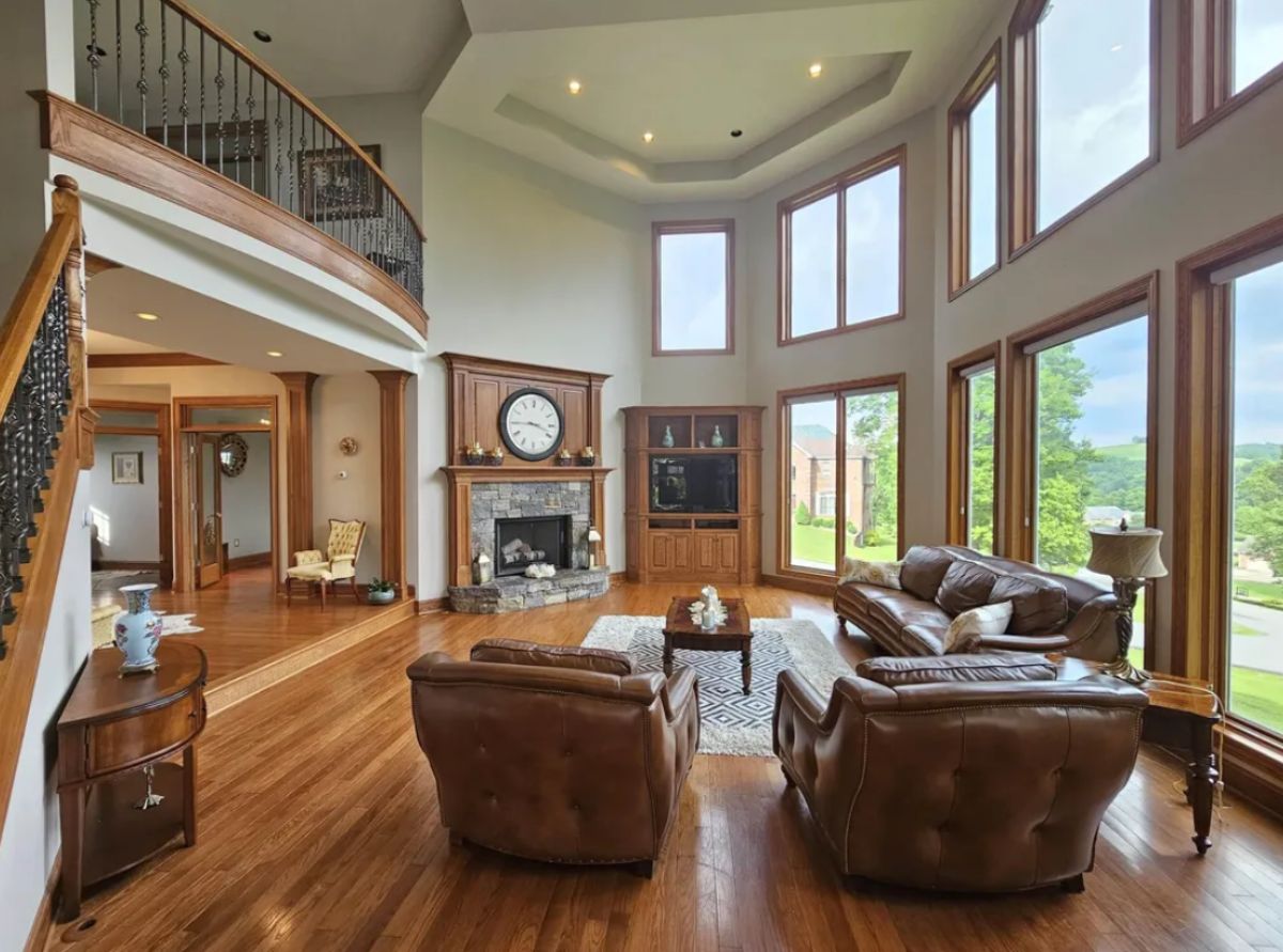 Living room with wooden floors, couches, large glass windows and a fireplace.