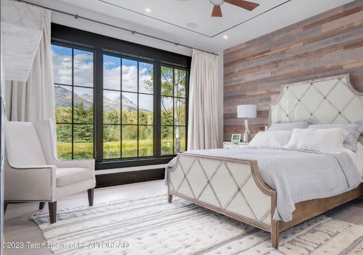 Bedroom with wooden floors, a large bed, and glass windows with a view of the mountains.