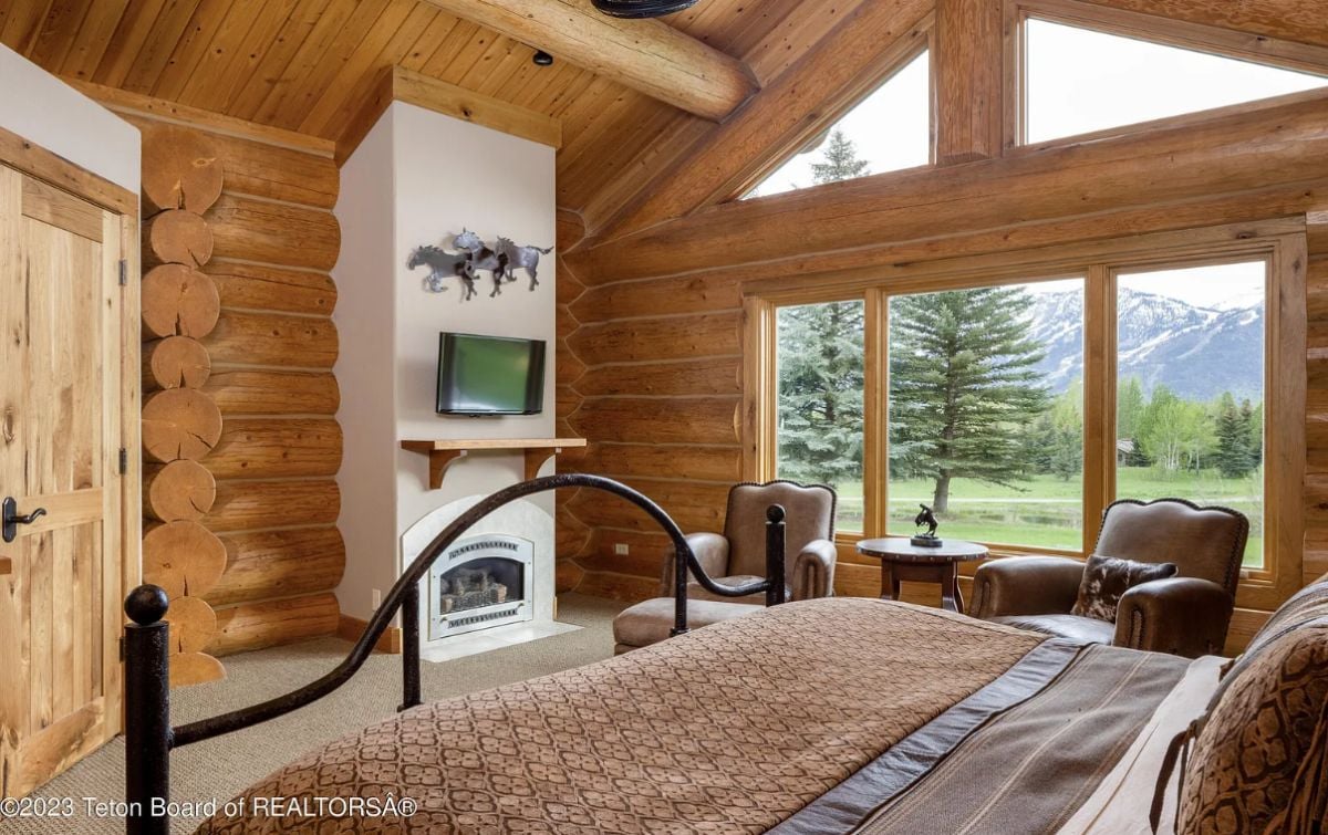Bedroom with a fireplace, carpet flooring, and glass windows with a view of the mountains.