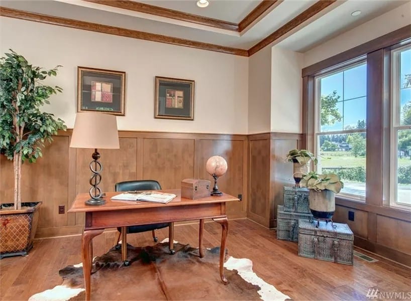 Study with half wainscoted walls, a tray ceiling, and a wooden desk over the cowhide rug.