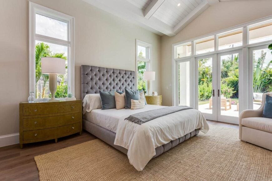 Large bed with a gray upholstered headboard and decorative pillows in a bedroom with large french doors
