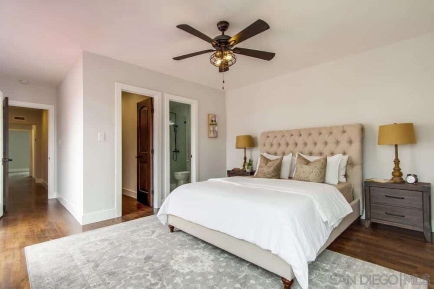 Large bed with a tan upholstered headboard in a bedroom with a gray rug