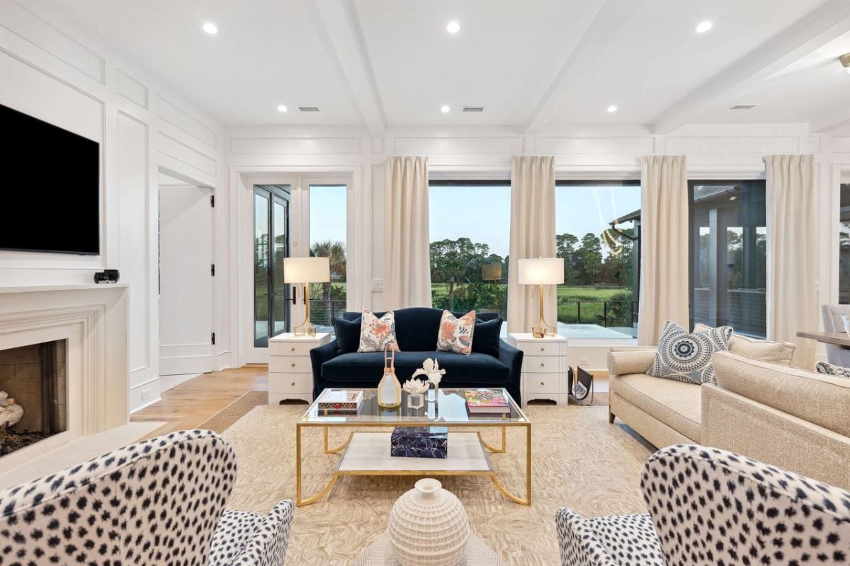 Living room with couches, a large rug, TV, glass wall windows and a fireplace.