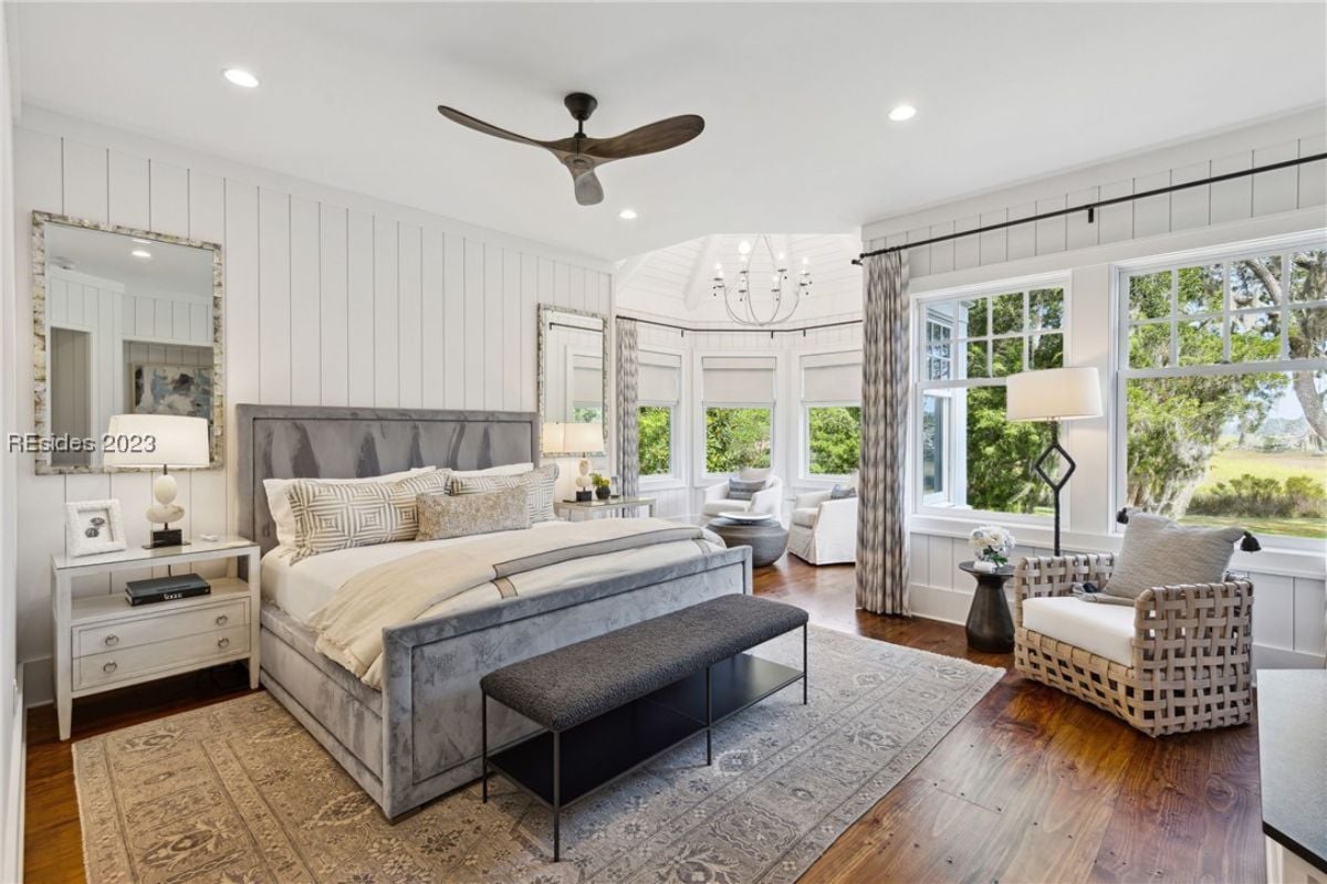 Bedroom with a large bed, couches, wood flooring and glass windows.