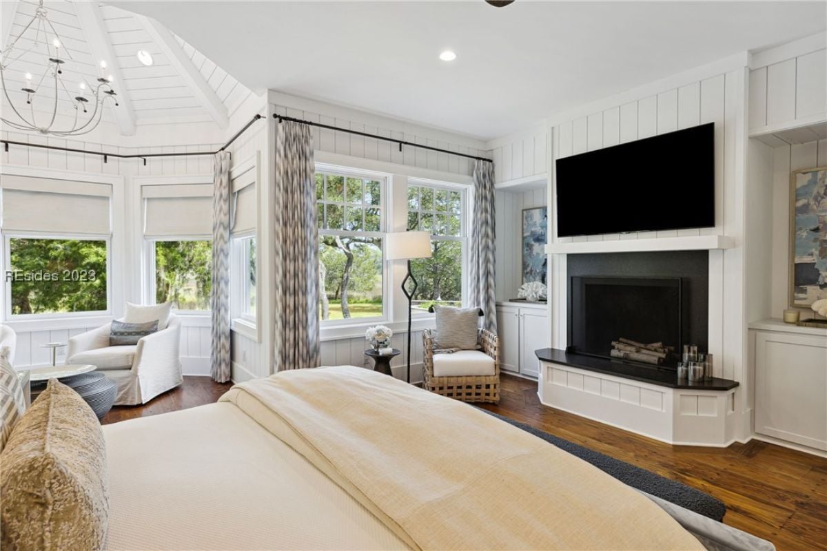 Bedroom with a large bed, couches, TV, fireplace and glass windows.