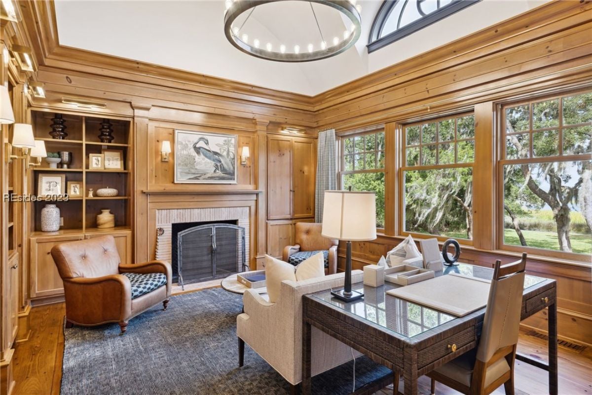 Home office with a desk, chairs, chandelier and a fireplace.
