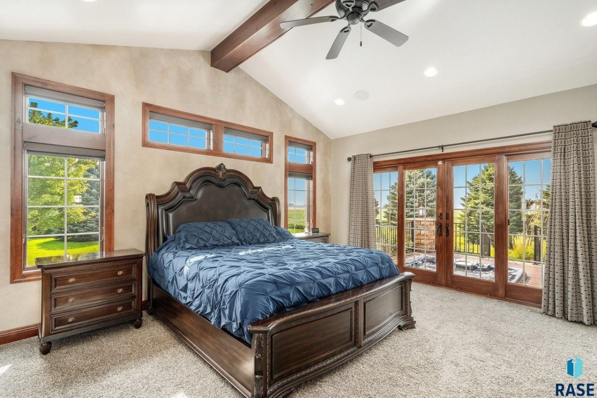 Bedroom with a large bed, carpet flooring, glass door and glass windows.