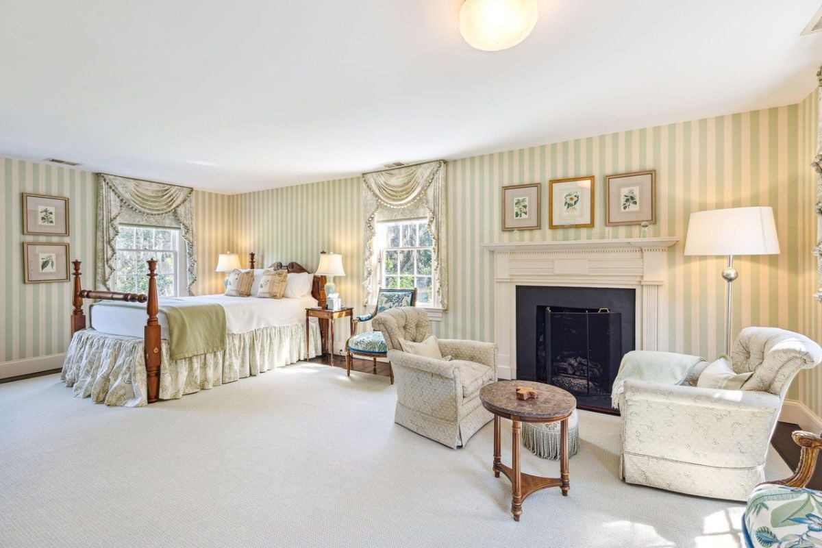 Bedroom with a large bed, carpet flooring, couches, fireplace and glass windows.