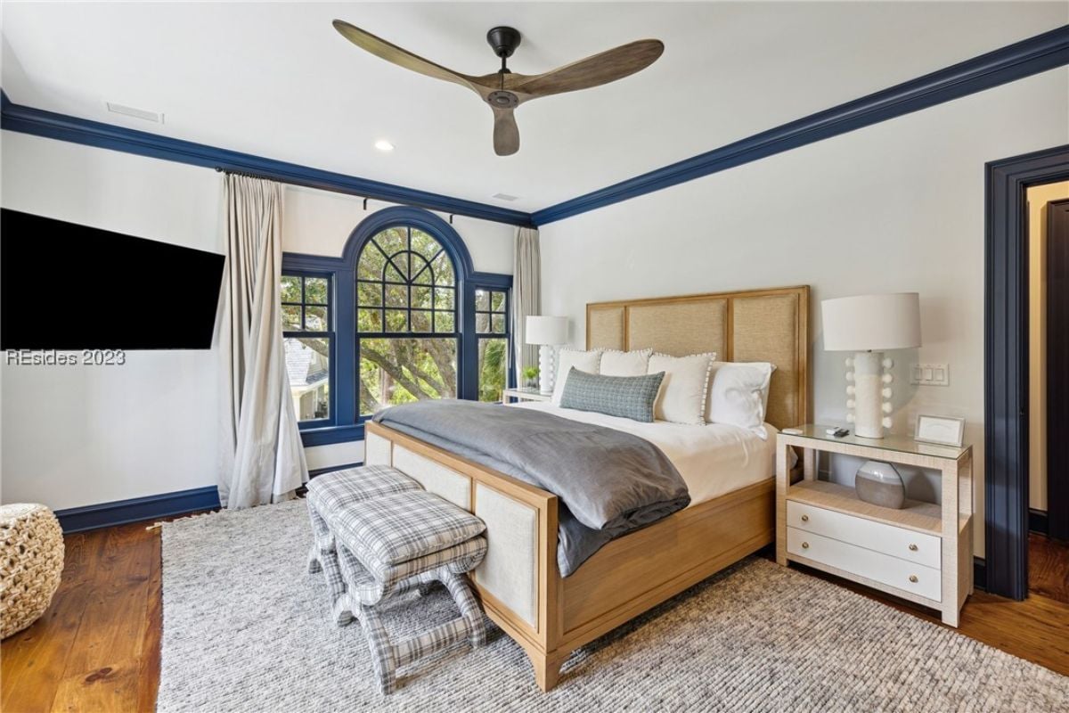 Bedroom with a large bed, ceiling fan, wood flooring and glass windows.