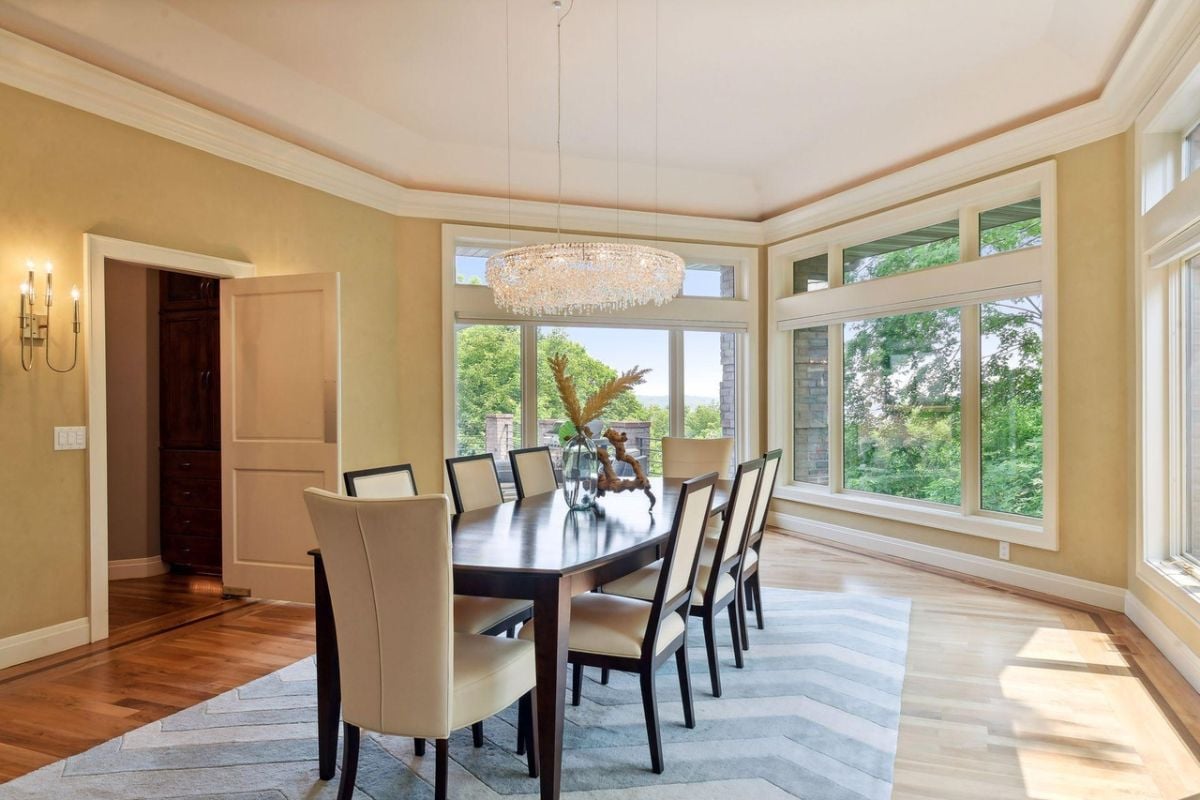 Dining room with a chandelier, wooden floors, a large rug, a large table and chairs.