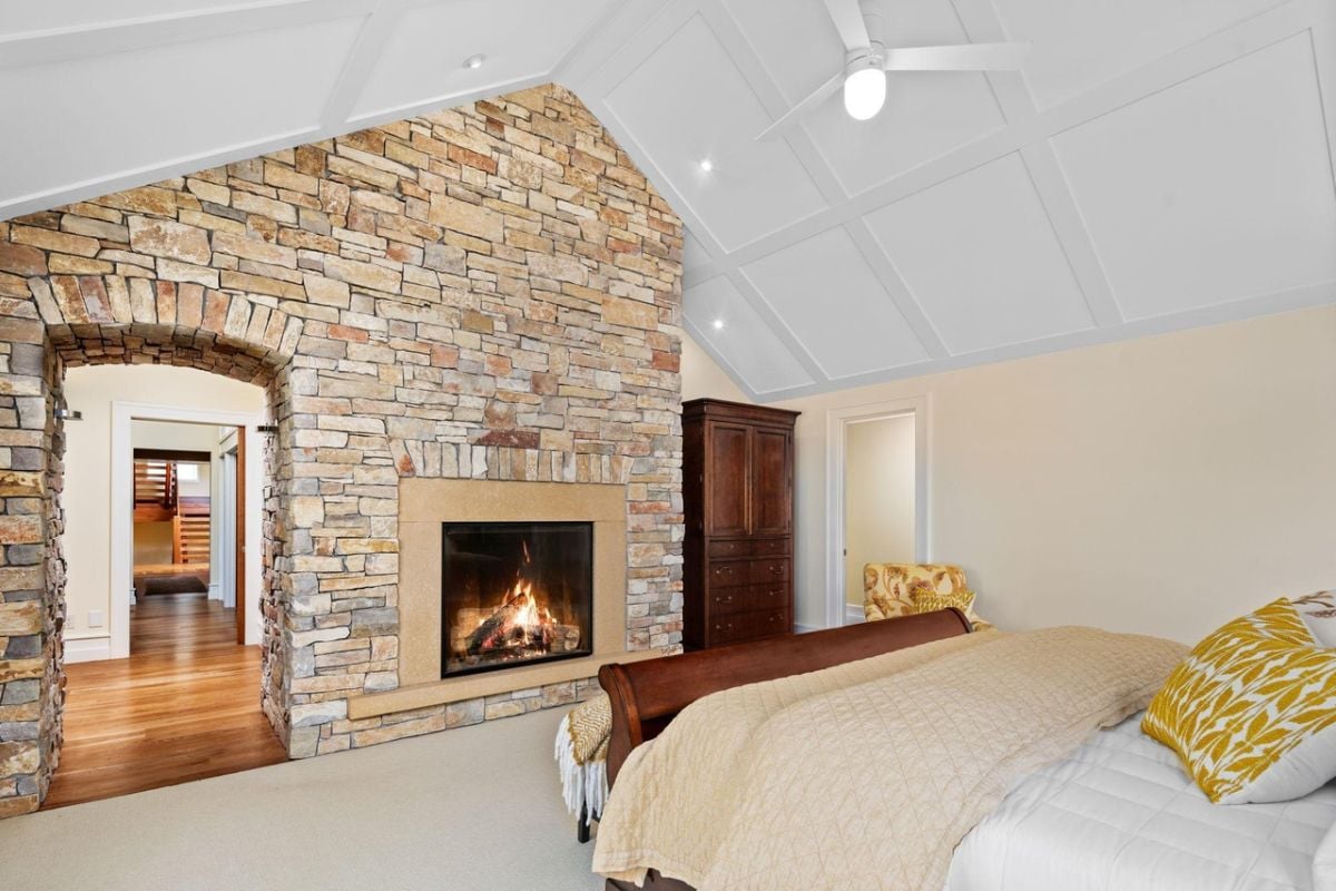 Bedroom with a large bed, carpet flooring and a fireplace.