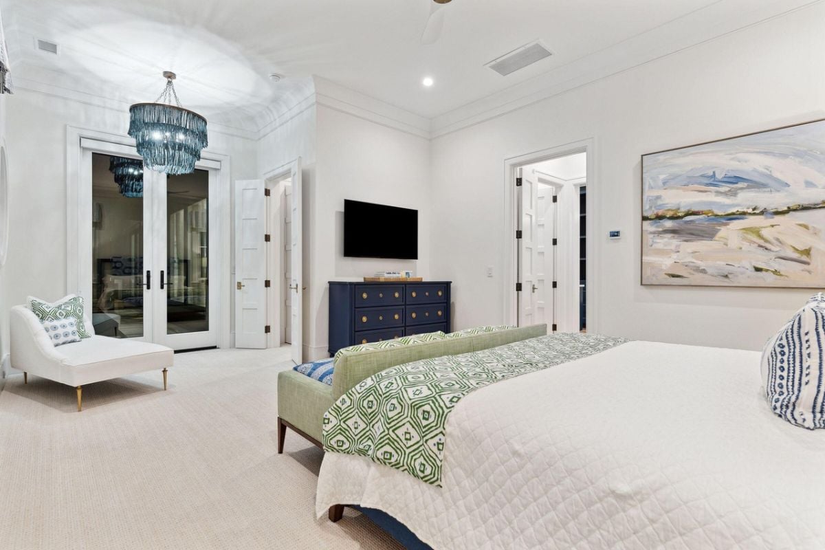 Bedroom with a large bed, carpet flooring, TV, chandelier and glass door.