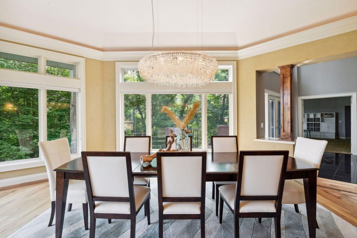 Dining room with a chandelier, wooden floors, a large rug, a large table and chairs.