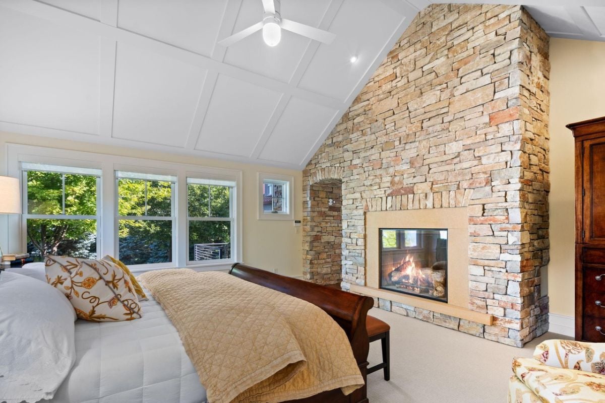 Bedroom with a large bed, carpet flooring and a fireplace.