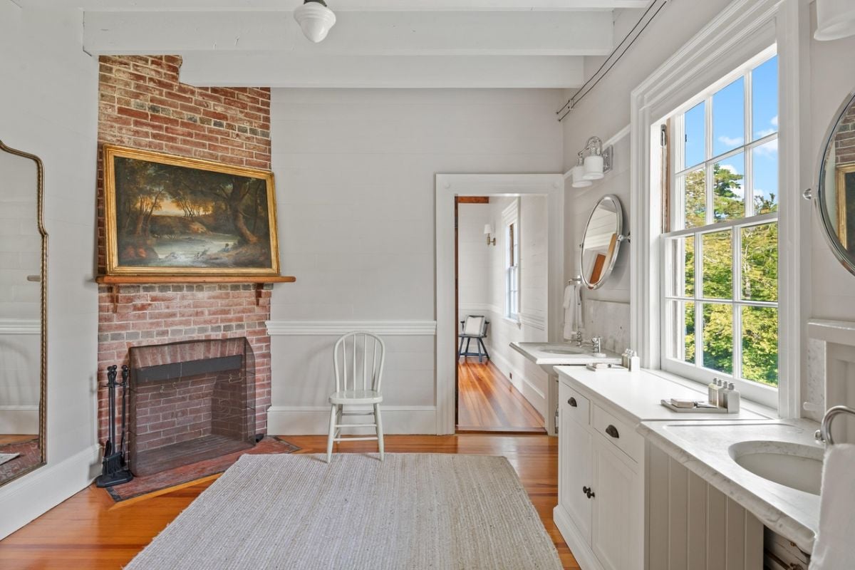 Bathroom with dual sinks, rug, wood flooring and glass windows.