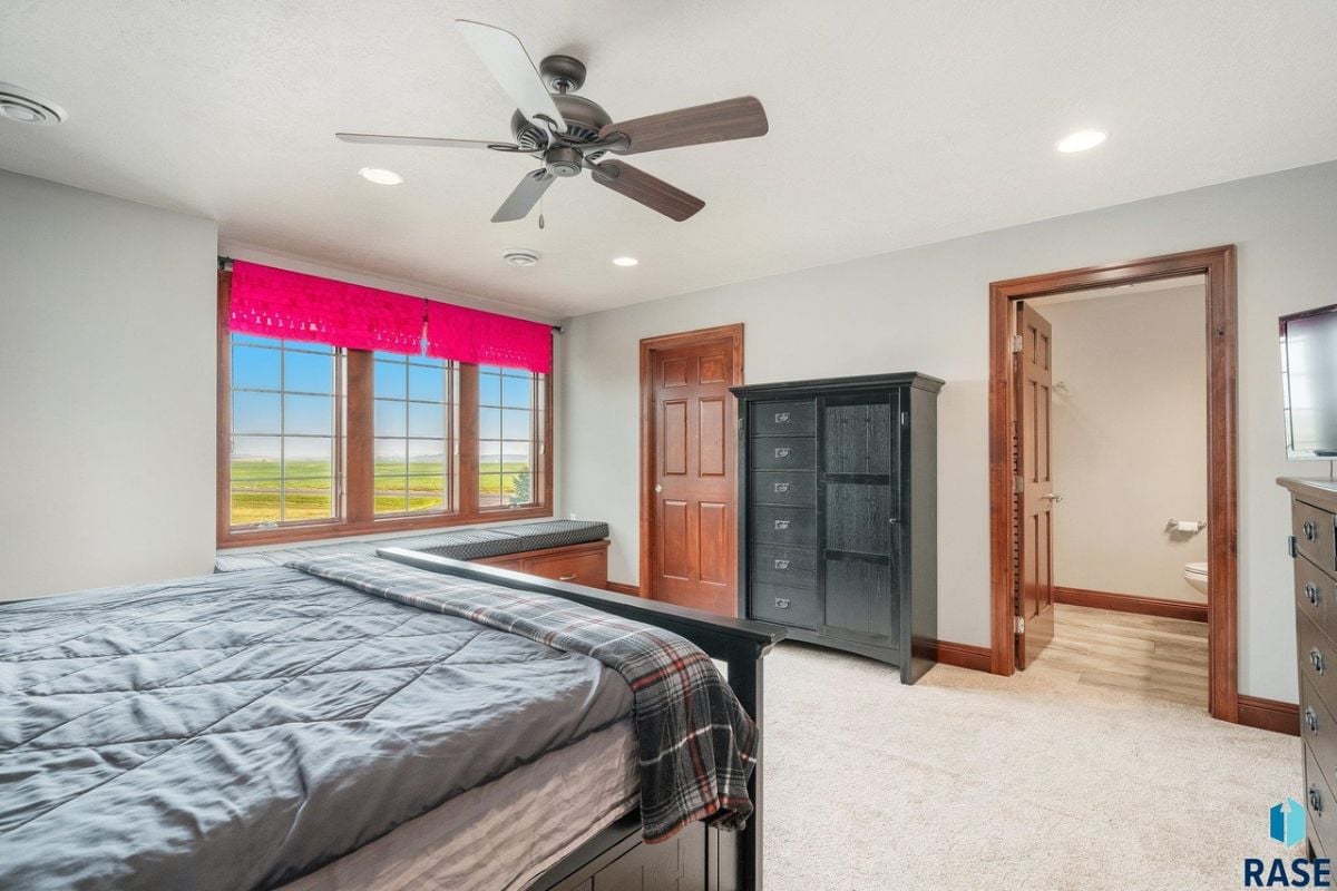 Bedroom with a large bed, carpet flooring, bathroom and glass windows.