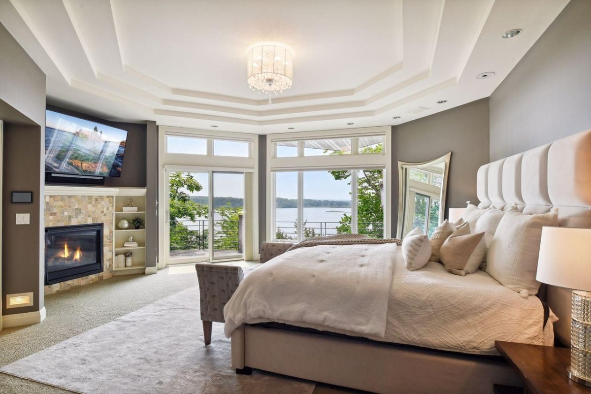 Bedroom with a chandelier, a large bed, TV, glass doors and a fireplace.