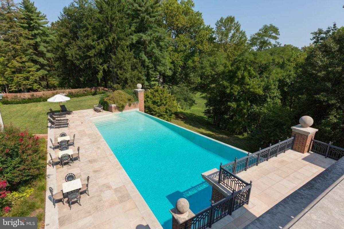 Pool with lounge chairs, tables and a green lawn.