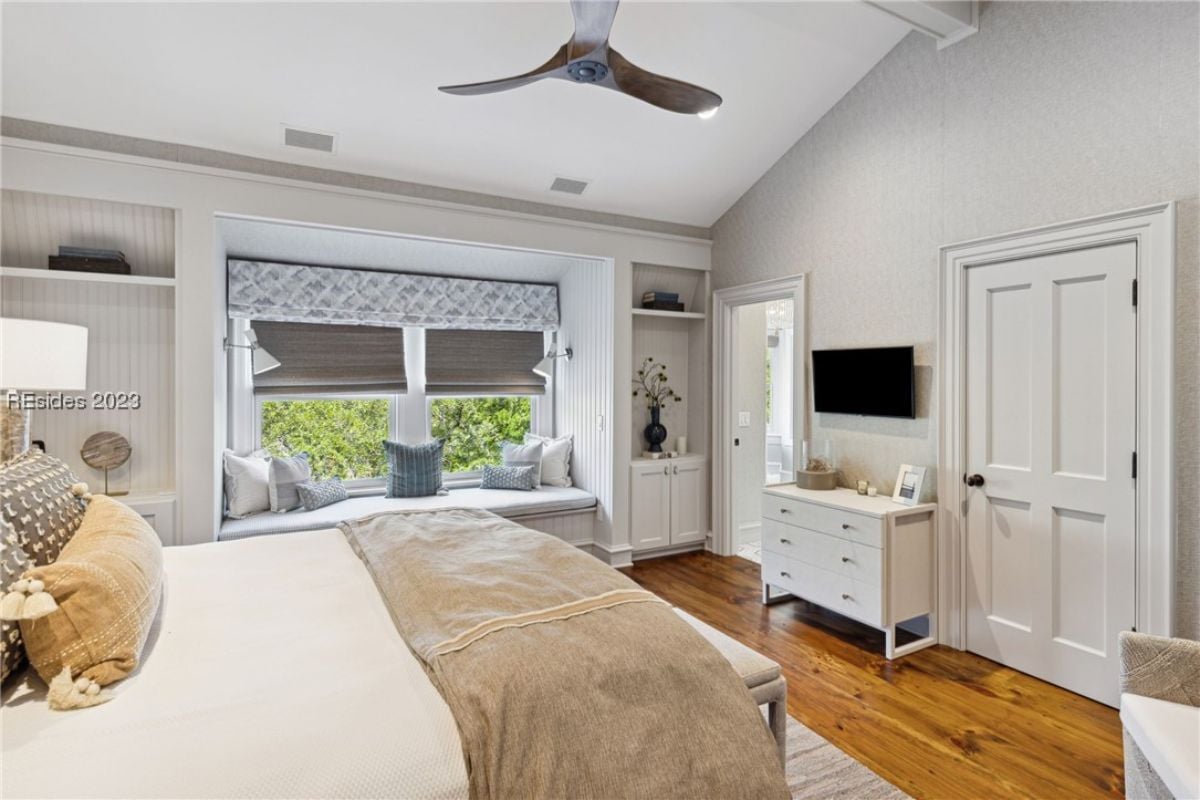 Bedroom with a large bed, ceiling fan, TV wood flooring and glass windows.