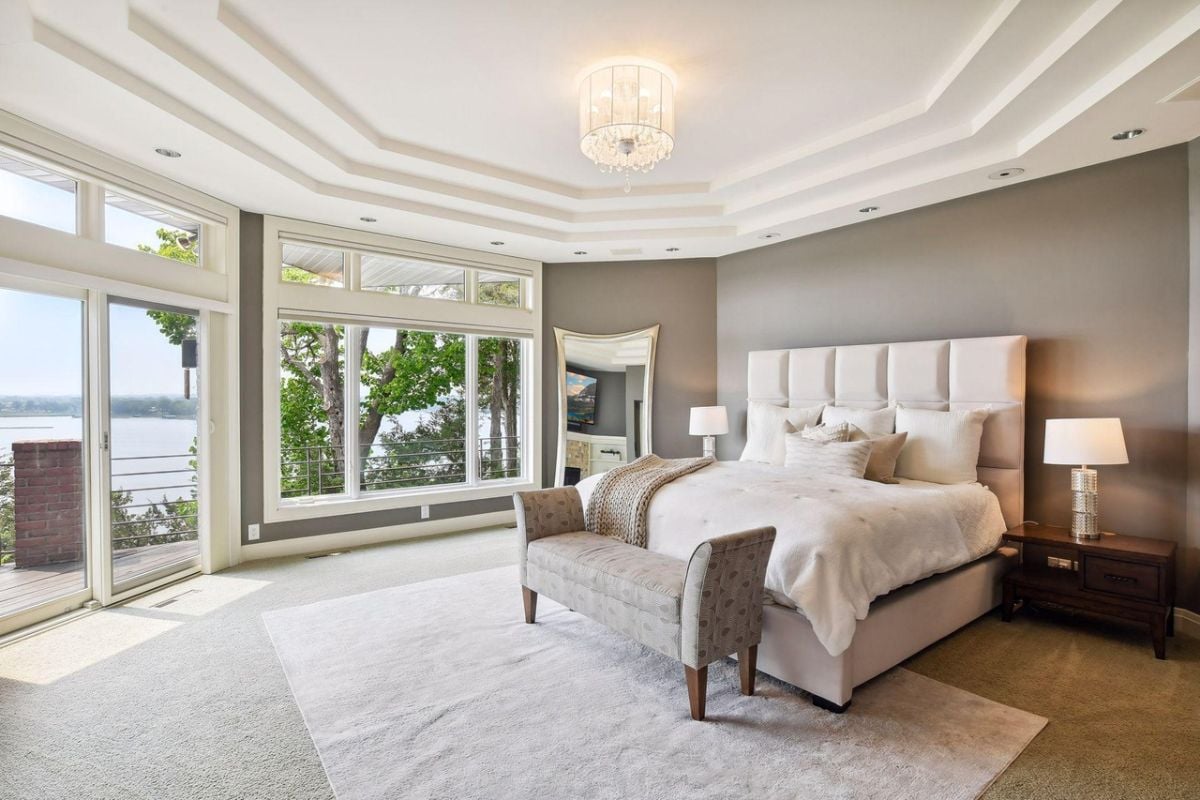 Bedroom with a chandelier, a large bed, TV, glass doors and glass windows.