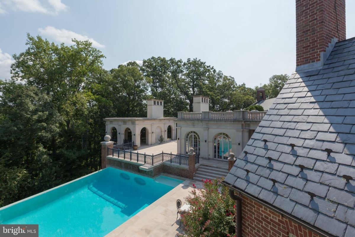 Pool with a balcony and trees in the background.