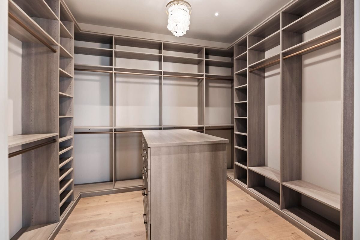 Walk-in closet with a chandelier and wooden shelves.