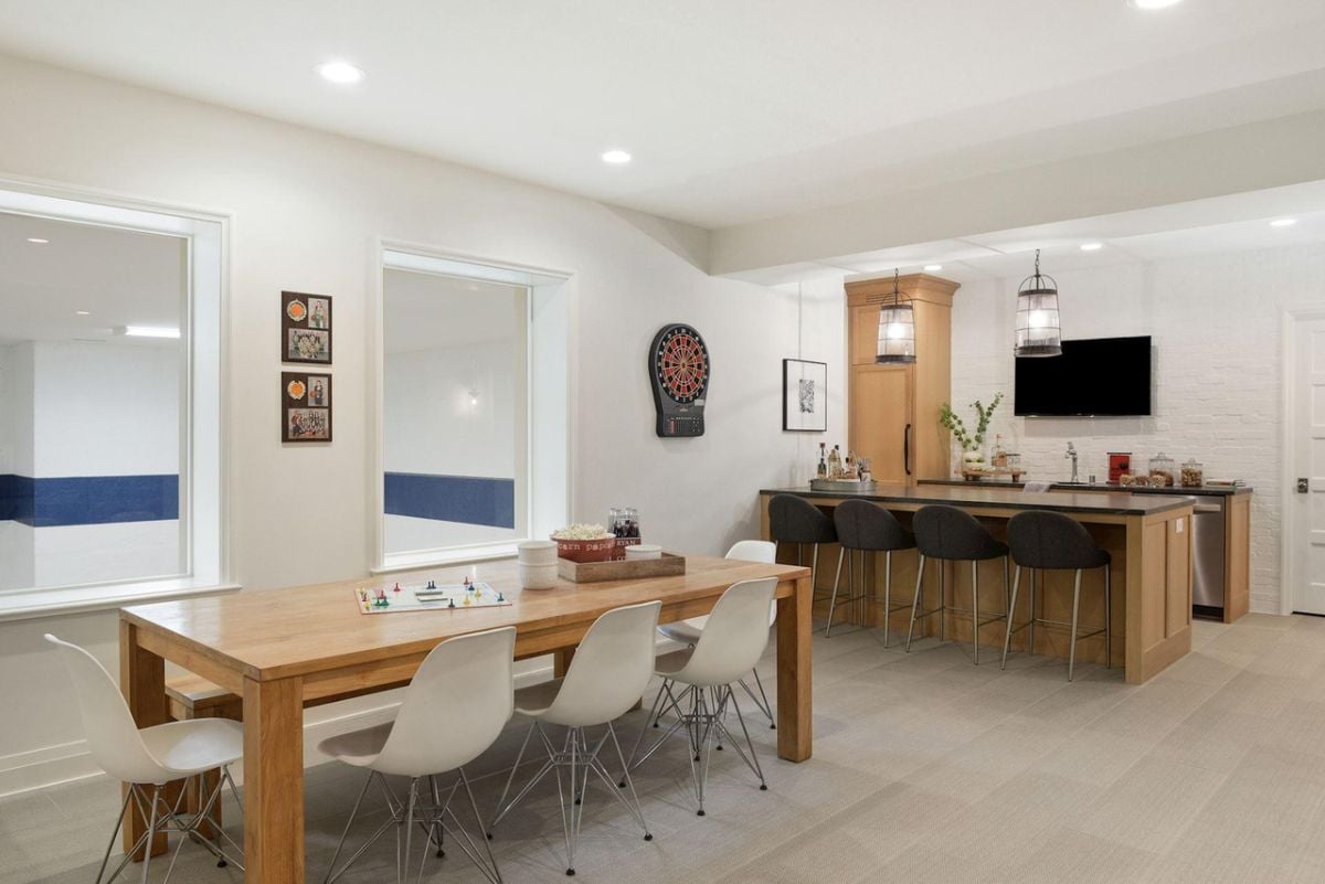 Recreation room with tile flooring, wooden table, chairs and a bar.
