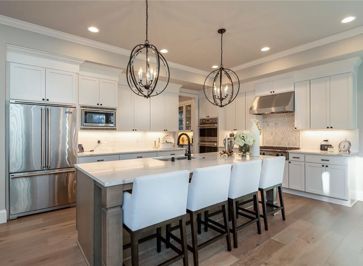 Kitchen with white cabinetry, stainless steel appliances, and a breakfast island illuminated by spherical chandeliers.