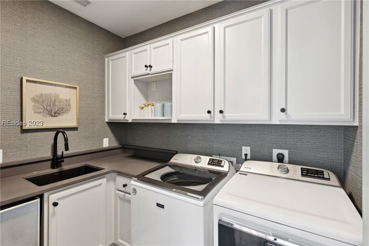 Laundry room with a sink, white cabinets, washer and dryer.