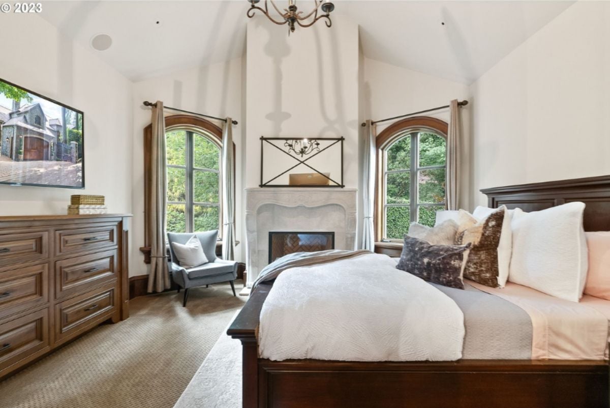 Bedroom with large bed, TV, carpet flooring and glass windows.