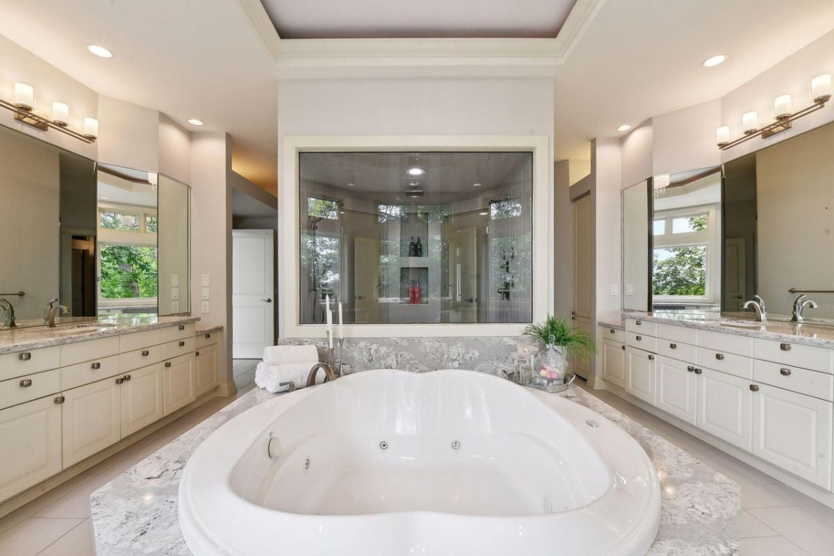 Bathroom with wooden white vanity, large mirrors and a soaking tub.