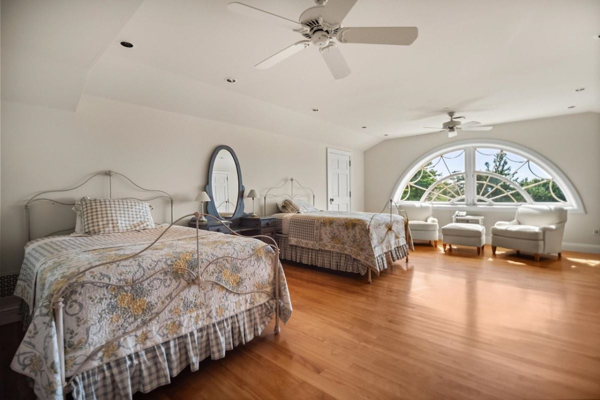 Bedroom with two beds, ceiling fan, wood flooring and glass windows.