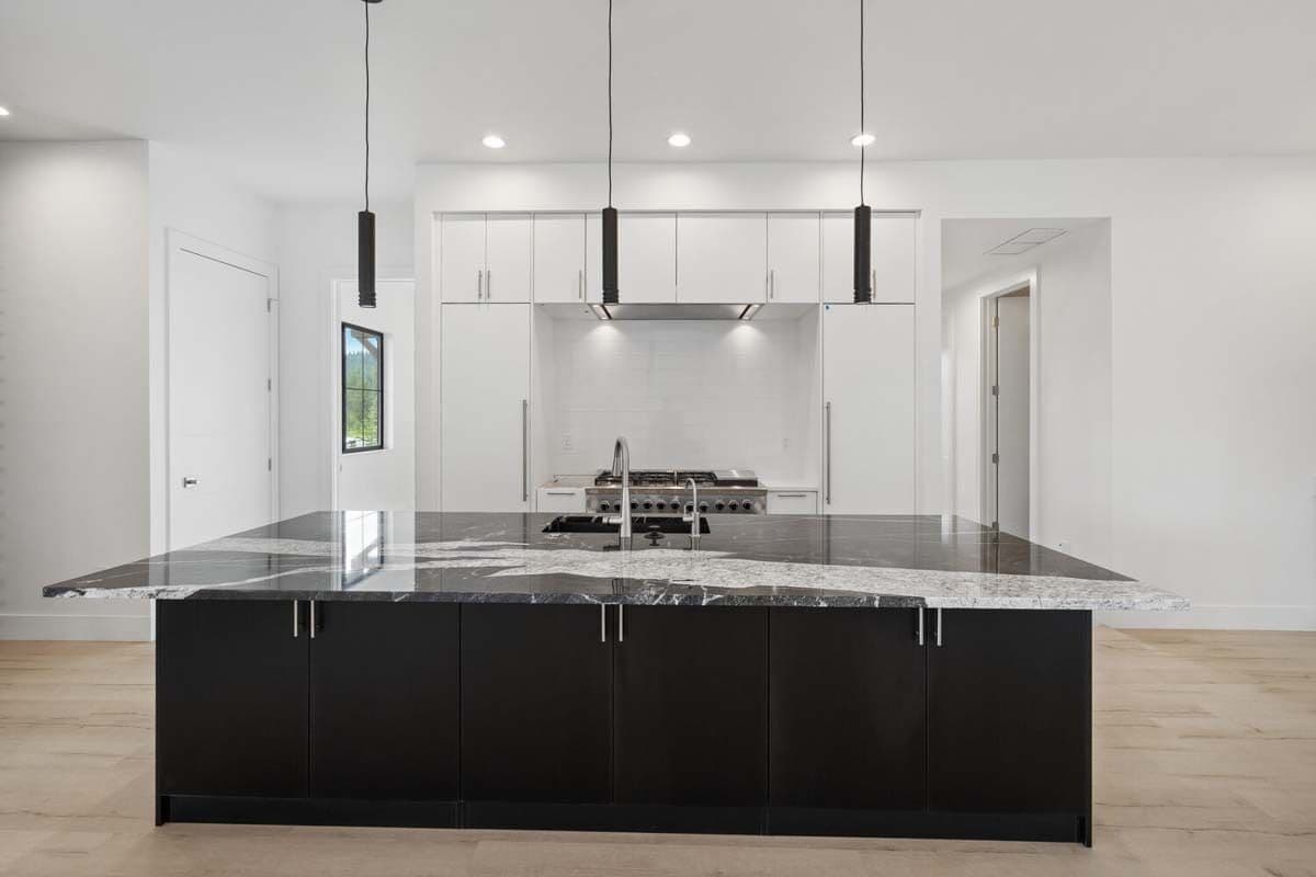 Kitchen with white cabinets and a contrasting island topped with cylindrical pendants.
