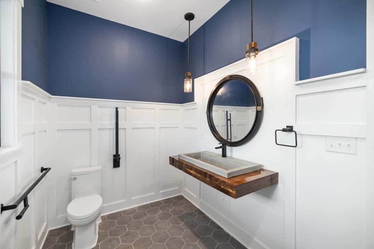 Powder room with blue and white wainscoted walls, hex-tiled flooring, and a floating sink topped with a round mirror.