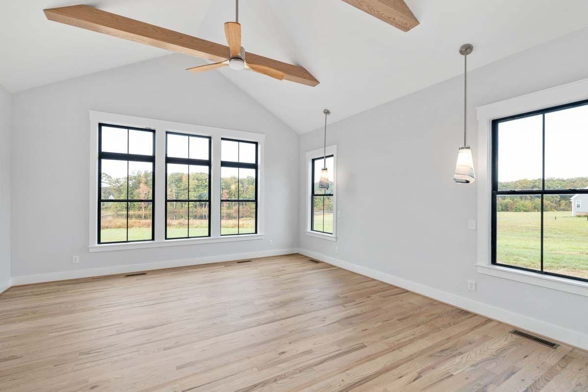 Primary bedroom with plenty of windows and a cathedral ceiling lined with exposed wood beams.