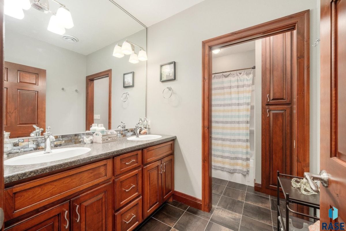 Bathroom with dual sinks, a large mirror and tile flooring.