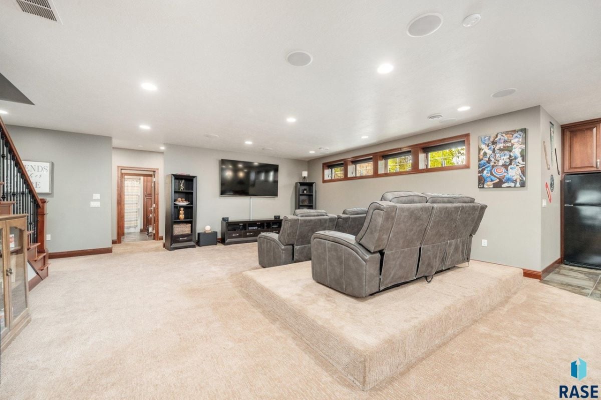 Media room with a large screen TV, carpet flooring, and couches.