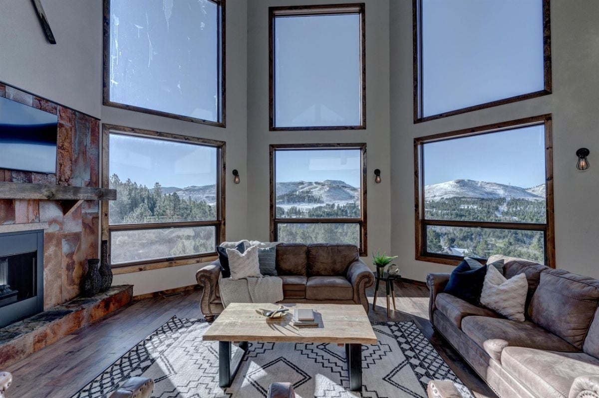 Living room with couches, fireplace, a large rug and glass wall windows.