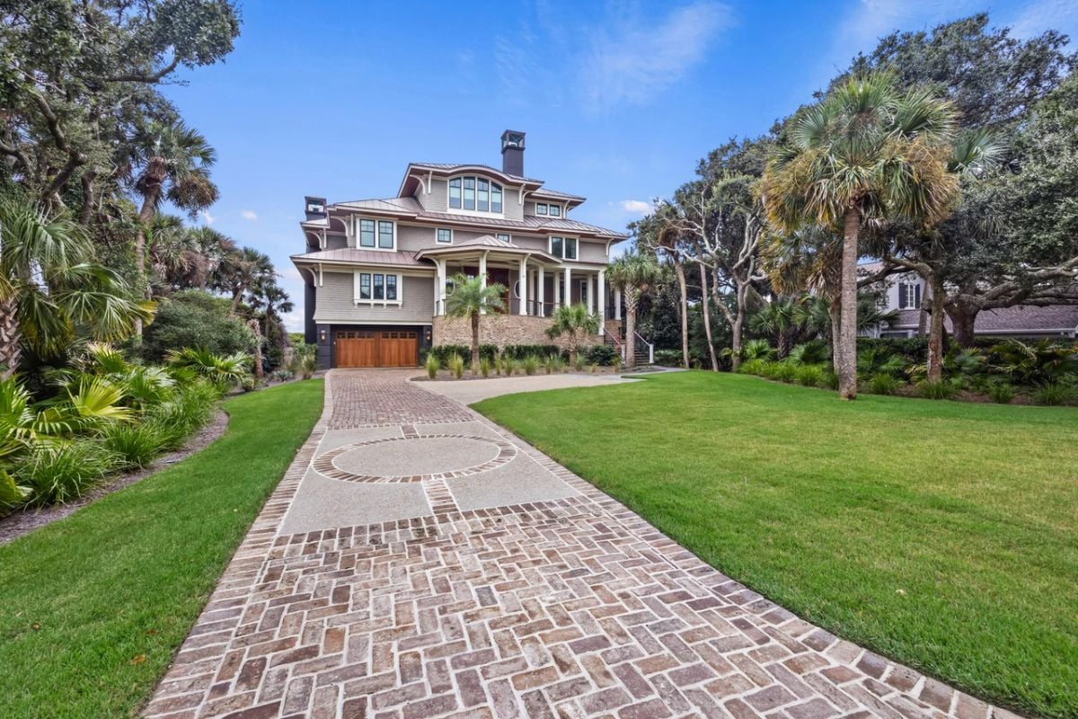 Front view of the mansion with a garage, spacious driveway and a large green lawn.