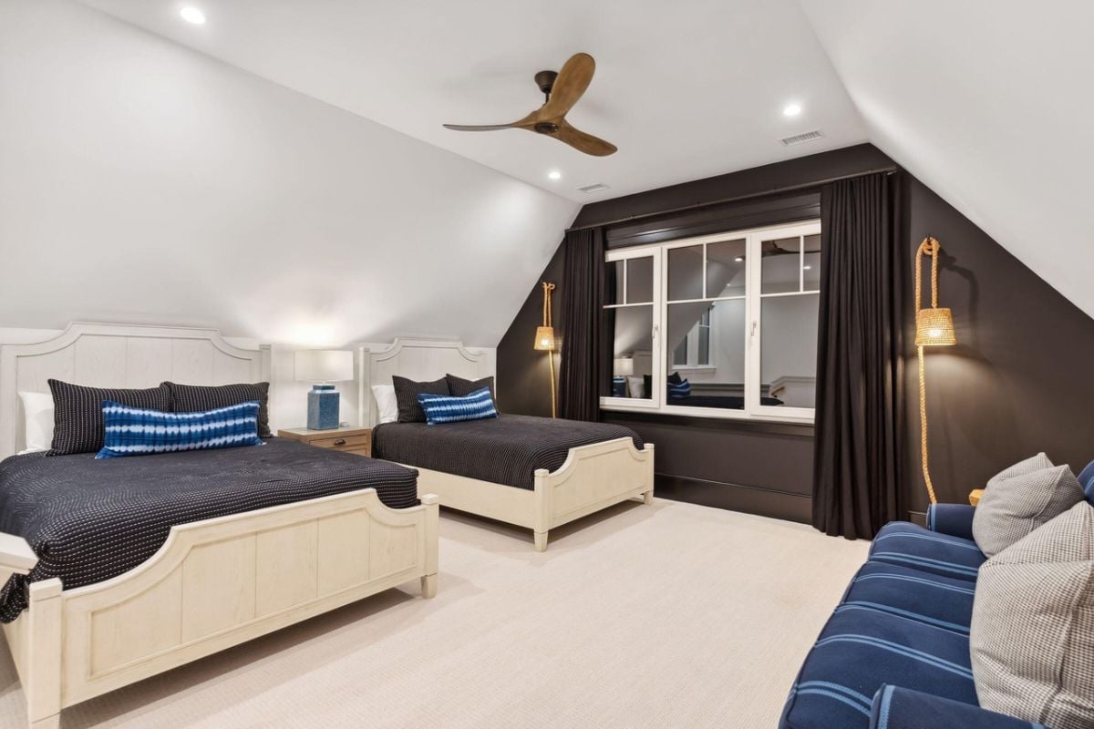 Bedroom with two beds, carpet flooring, ceiling fan and glass windows.