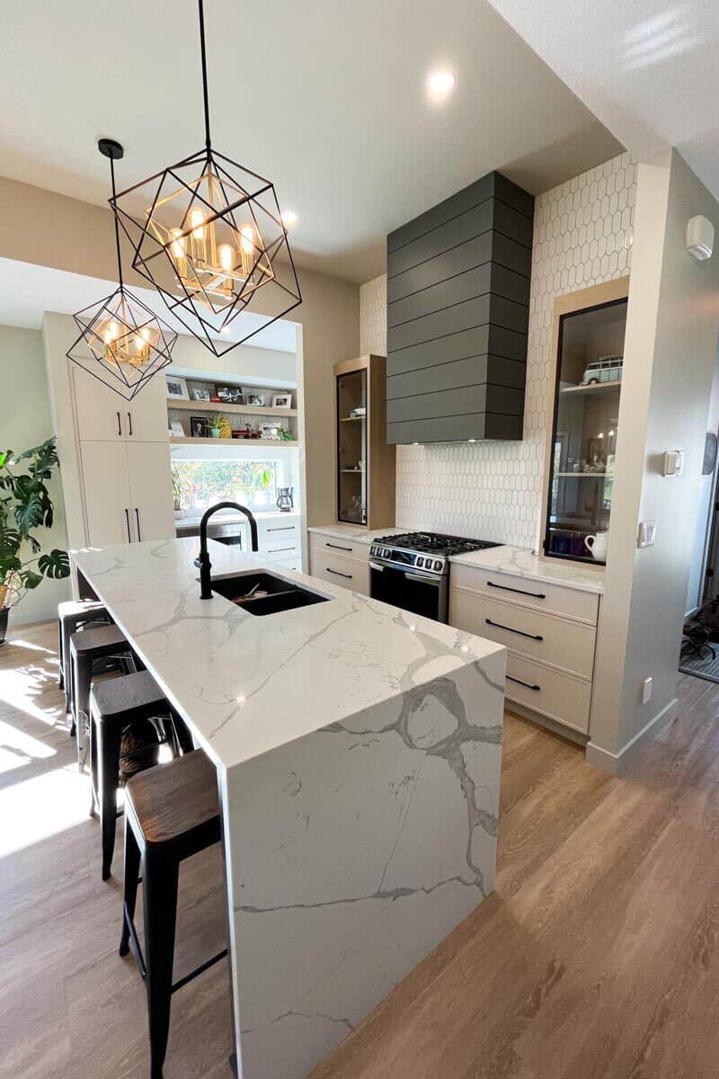 Kitchen with white cabinets and a waterfall island with double sinks and bar seating.