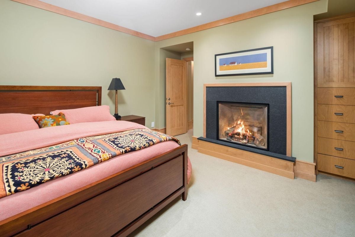 Bedroom with a large bed, carpet flooring and a fireplace.